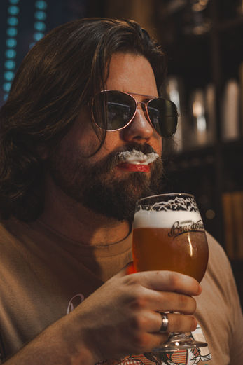 Homem de óculos escuros com espuma de cerveja no bigode.