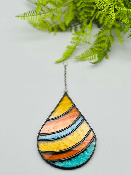 Colorful stained glass teardrop earring with various horizontal stripes and green leaf background.