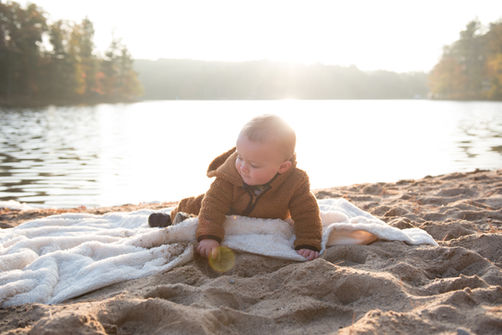 baby sitting on a blanket at the beach in front of lake arbutus
