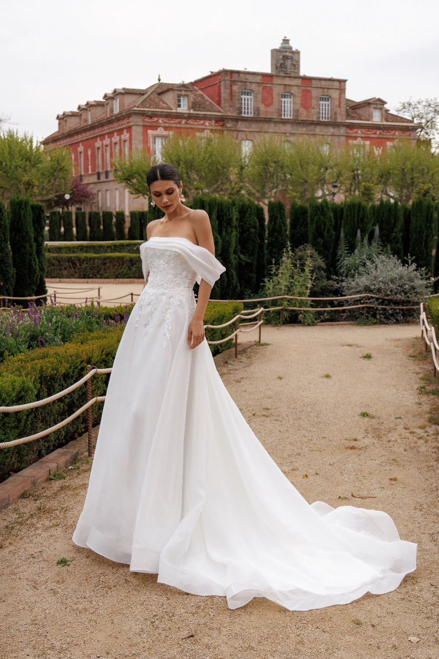 Femme en robe de mariée blanche à longue traîne, devant un château.