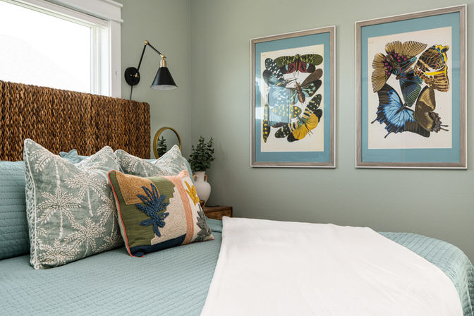 comfy bed with blue comforter and white throw blanket , and 2 pictures of butterflies above in an airbnb