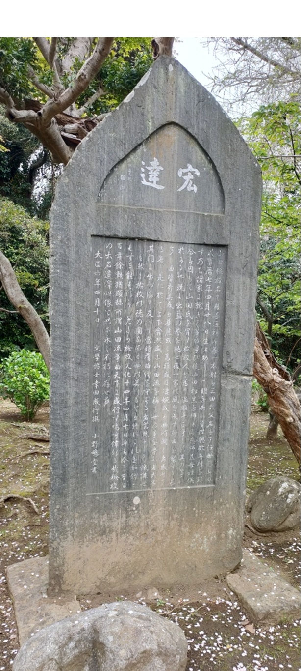 縦長の大きな石碑の写真。石碑は尖頭アーチ(尖ったアーチ型)の上部を持ち、そこには白文字で「宏達」と右から左へ横書きで大きく刻まれています