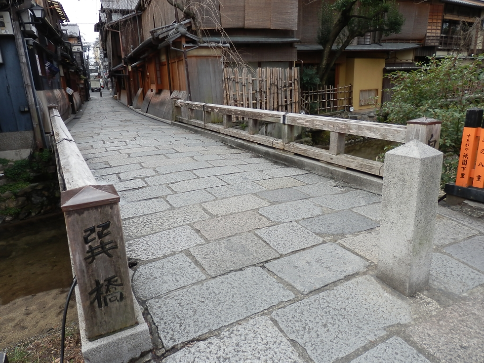 祇園白川の巽橋。木製の手すりが特徴的な石造りの小さな橋が手前にあり、奥には情緒あるお茶屋建築と石畳の路地が続いている。