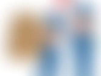 青い作業服を着た工場勤務者が重い段ボールを抱えて苦しそうにしている様子。隣には腕を組んで怒った表情の同僚が立っている