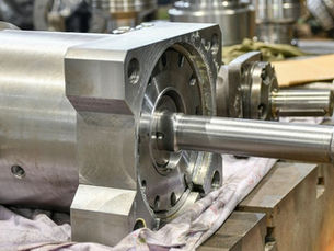 Large hydraulic component with machined flange and drive shaft on a workshop bench
