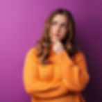 Young woman in an orange jumper with a thoughtful expression, representing curiosity about the differences between Ozempic and Mounjaro.
