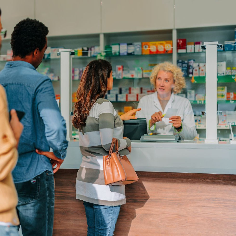 A pharmacist speaking with a customer across the counter while others wait in line inside a busy UK pharmacy.