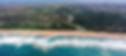 Aerial view image of Zimbali Coastal resort which includes the ocean with waves crashing on the beach leading up to a view of the lush forest with holiday homes nestled on the hillside