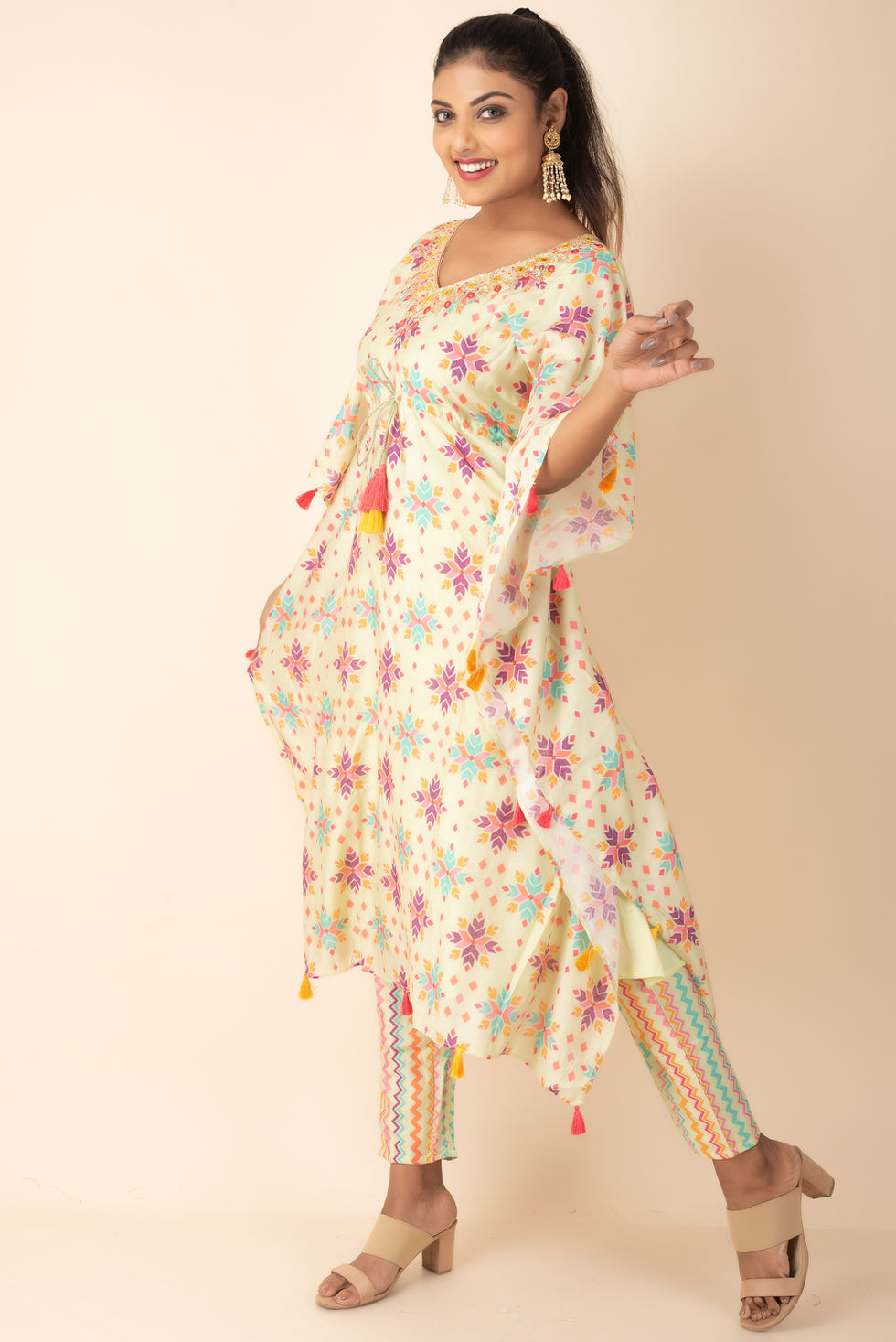 a woman is wearing a colorful dress with tassels on the sleeves