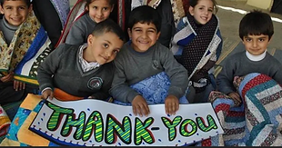 Children sit covered in quilts and holding a thank you banner