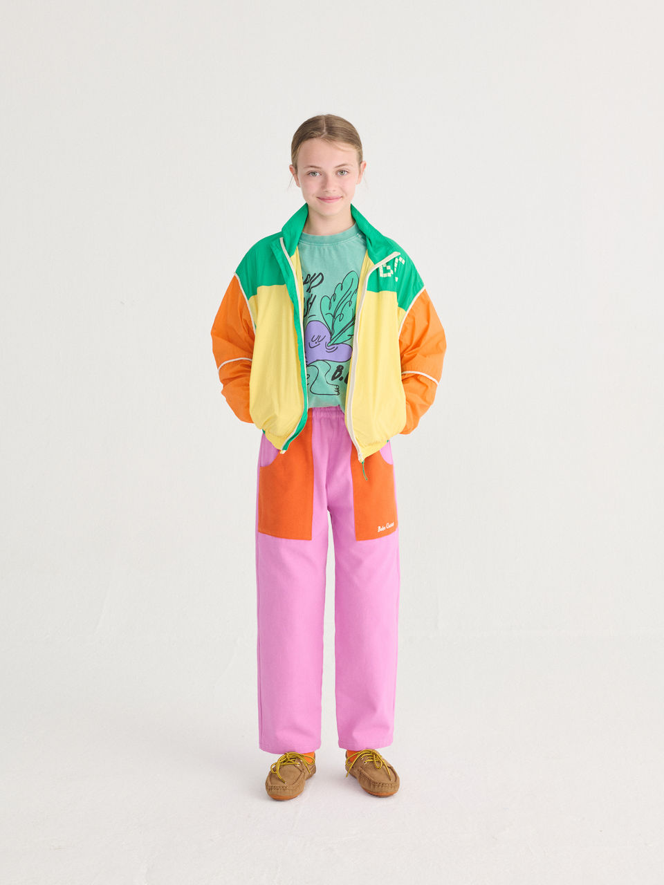 Child wearing pink and orange pants with a green T-shirt and a color-block jacket.