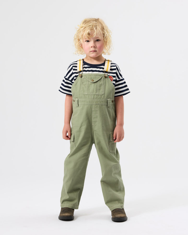 Child standing and facing forward, wearing olive green overalls over a striped T-shirt.
