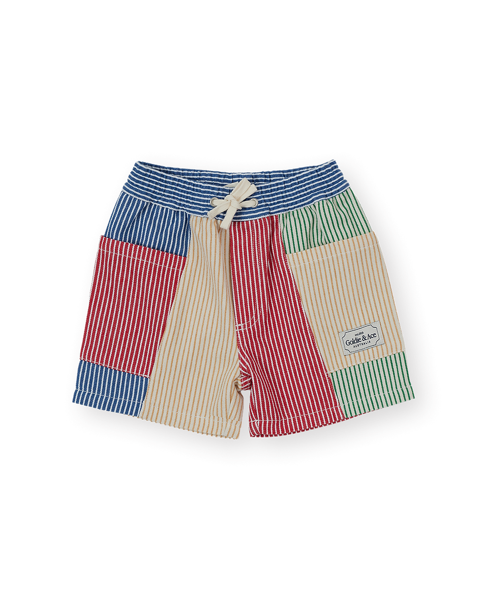 Multicolored children’s shorts with mixed vertical stripe panels in red, blue, green, and beige, featuring an elastic waistba
