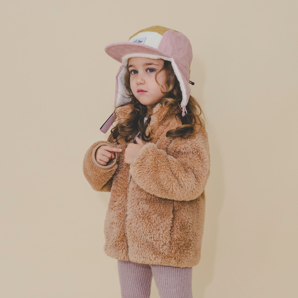 Girl posing frontally in brown faux-fur jacket and pink Lil’ Boo cap with ear covers.