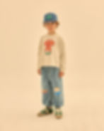 Child wearing blue denim pants with a light long-sleeve shirt and a cap, standing against a neutral background