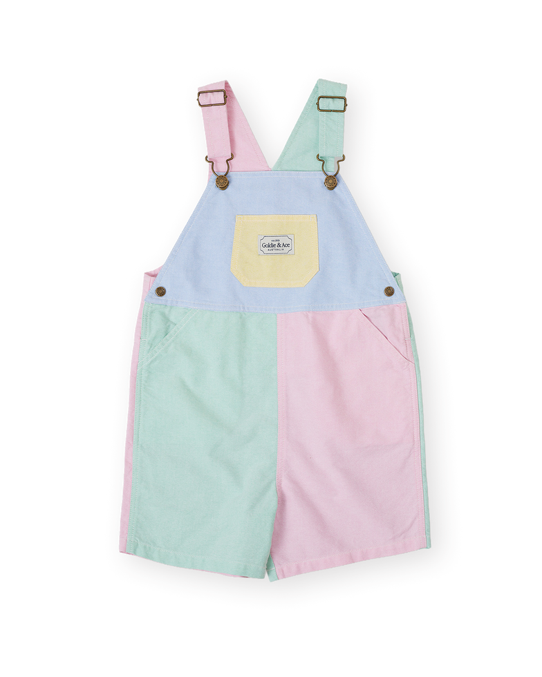 Pastel color-block children’s short overalls with pink, mint, and blue panels, adjustable straps, and a front pocket.
