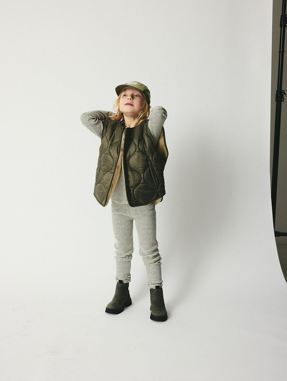 Child wearing the reversible vest with a relaxed outfit, hands behind the head.