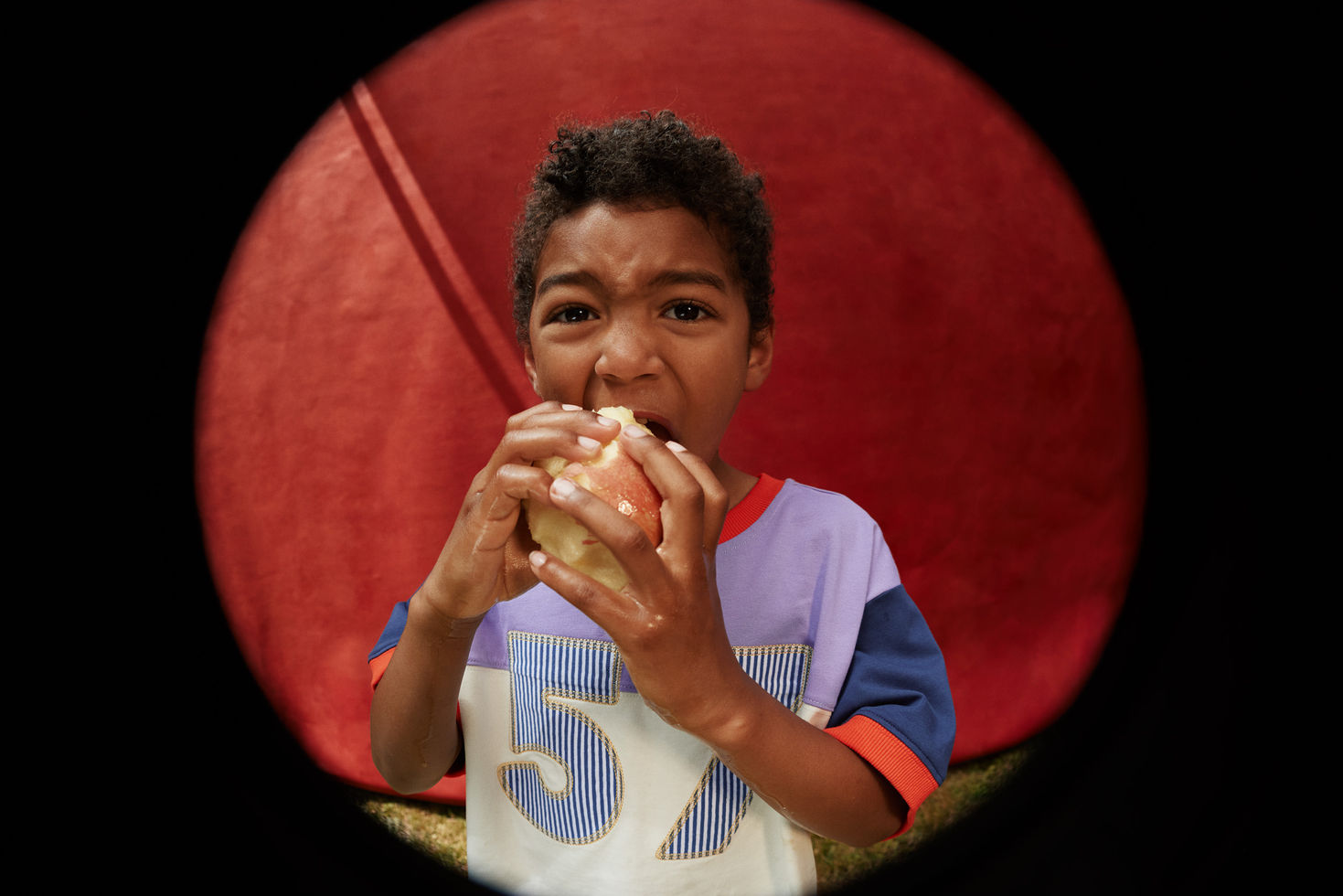 Close-up of a child eating a sandwich, wearing the “57” T-shirt against a red circular background.
