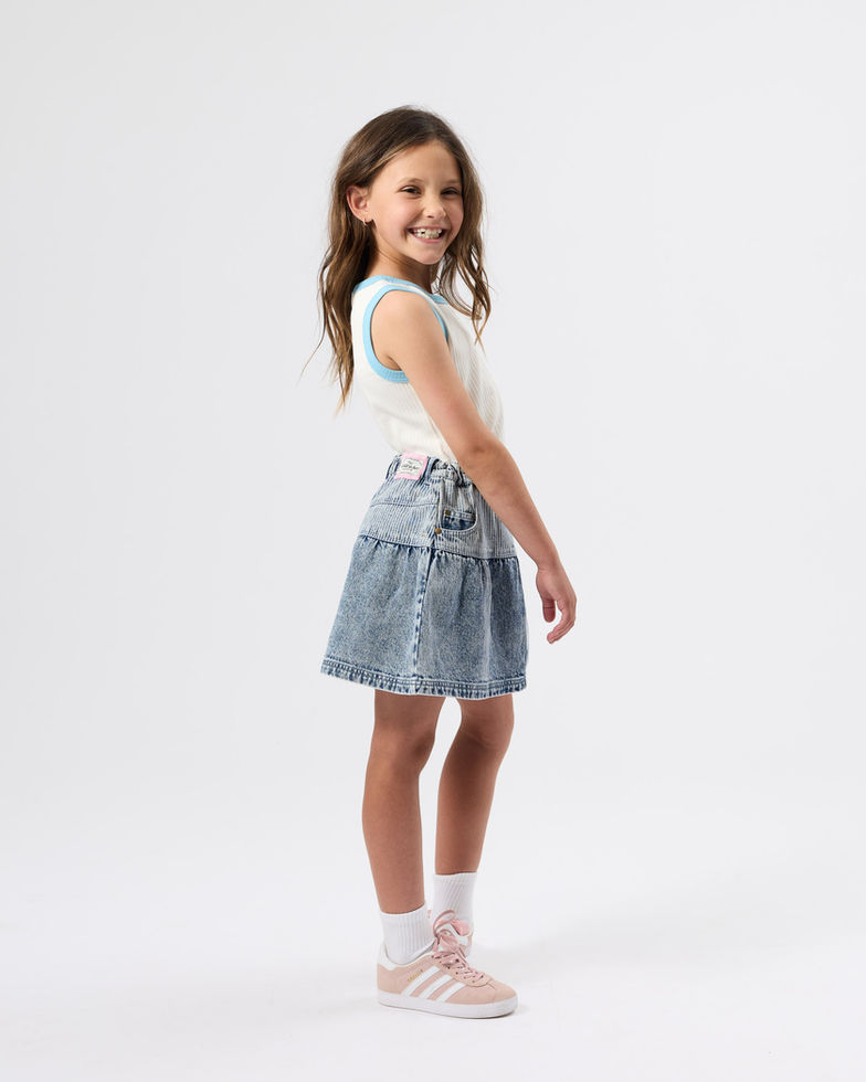 Girl turned slightly to the side, smiling, wearing the cream tank top with blue trim and a denim skirt.