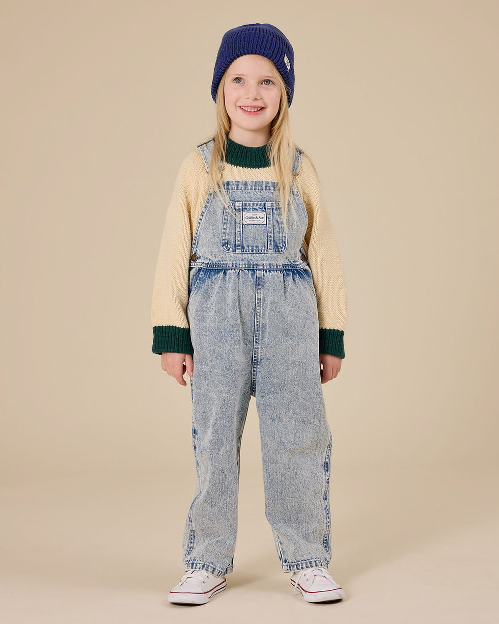 Child standing and facing forward, wearing light blue denim overalls over a long-sleeve top.