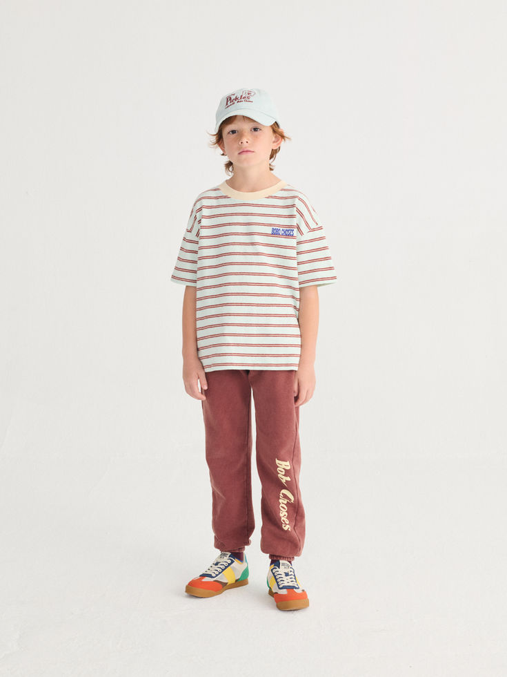 Child wearing brown sweatpants with a striped T-shirt and cap.