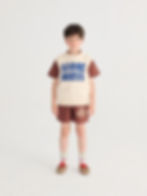 Child wearing a beige knitted vest with blue text paired with brown shorts.