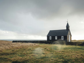 A lonely church in the middle of a eerie field with the sun setting behind