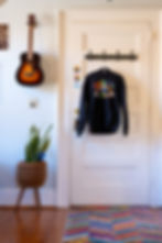 Welcoming corner at Resonance Center featuring a door with a 'Therapy is Cool' sweatshirt on a hook, a vibrant rainbow rug, a potted plant, and a guitar hanging on the wall, creating a warm and inviting atmosphere.