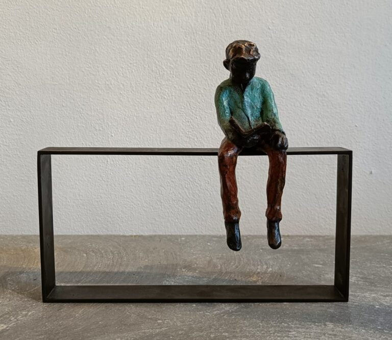 Bronzen beeldhouwwerk 'Studeren op hekwerk' door Cher Mattijssen, een jongen die op een hekwerk leest, op JolienVerhaegen.nl