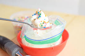 Spoon with ice cream and sprinkles over a ziplock bag in a red bowl. Bright and cheerful kitchen setting. Calories not shown.