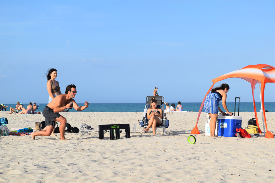 Outdoor game beach SLOTS rolling wheel game best yard fun thing to do black and green tire through slot opening at the beach outside games family friendly easy fun most addicting all ages adult games grass yard outdoors sport sand group of people