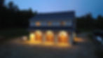 Twilight aerial photo of a 3-bay carriage house garage with warm lit windows, central Maine