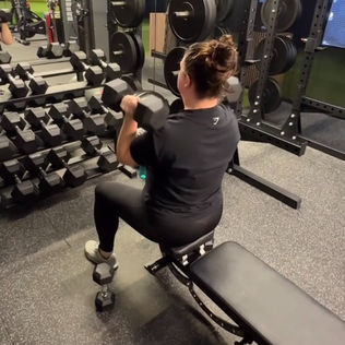 female client performing a seated on a bench dumbbell press