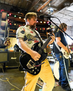 Musician playing a black electric guitar on stage.