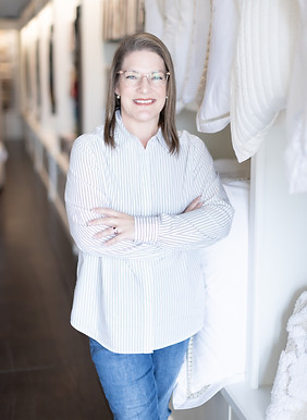 Kimberly Jones, Interior design professional smiling with arms crossed in a luxury textile showroom, surrounded by crisp white linens and curated fabrics.
