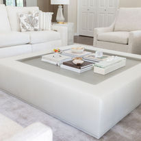 Oversized upholstered coffee table styled with designer books and decorative accessories in a luxury family room.
