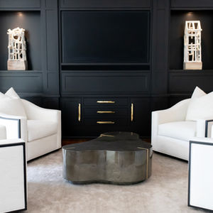 Sophisticated black and white sitting room by Birdy Design, featuring four white club chairs with black trim, abstract bronze coffee table, built-in black cabinetry with gold hardware, and modern sculptural art displays.