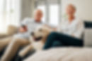 Older couple sitting on couch with dog watching television.