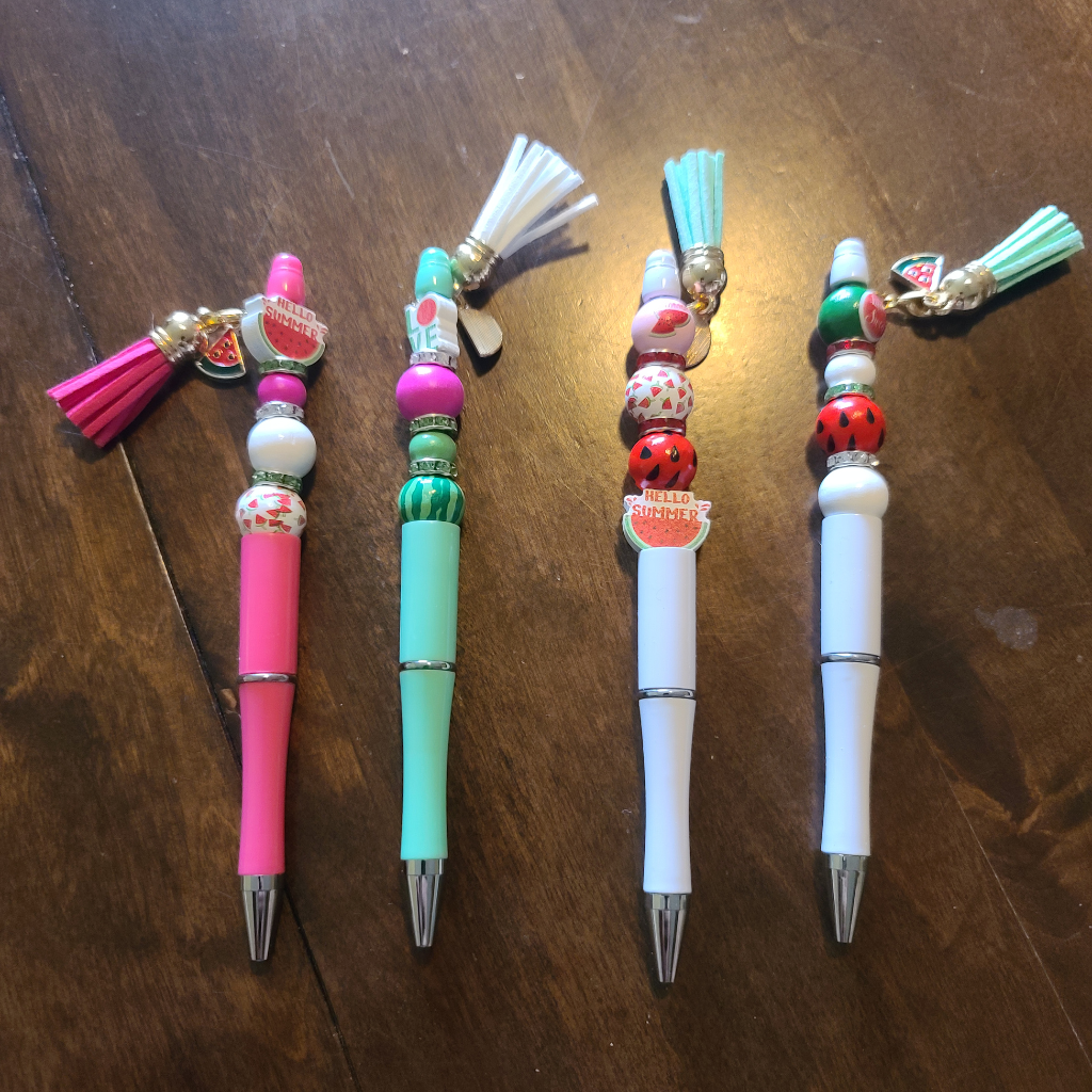 Four handmade beaded pens featuring watermelon focal beads, charms, and colorful tassels.