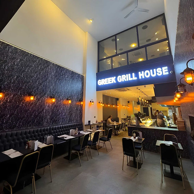 Interior of a modern Greek grill house restaurant with seating, warm lighting and open kitchen.
