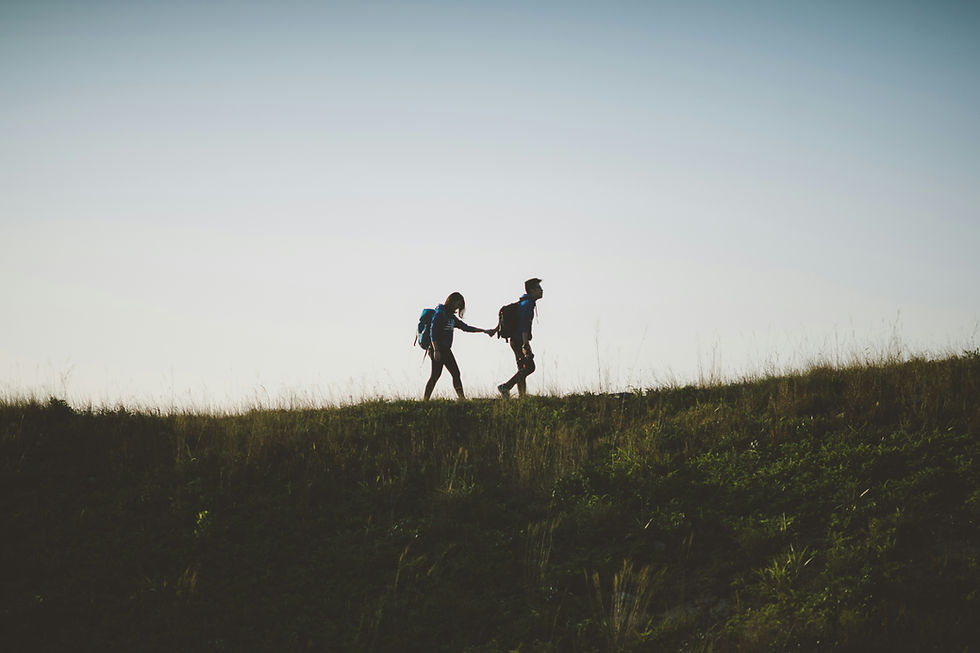 Zwei Personen wandern. Die vordere Person nimmt die Hintere an die Hand und führt und unterstützt sie. Foto von Joseph Chan auf Unsplash