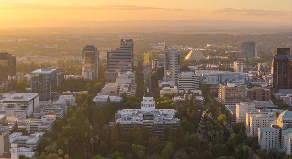 Aerial view of a cityscape during sunset, featuring a prominent white domed building, surrounded by tall buildings and lush greenery.