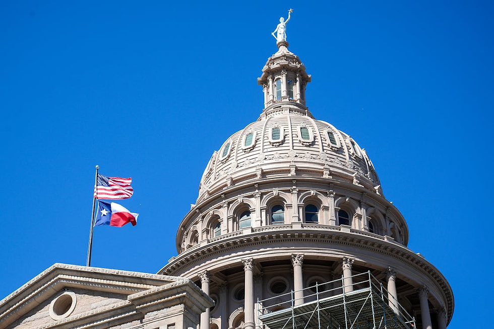 Dome of a capitol building with American and Texas flags waving. Clear blue sky, scaffolding visible below the dome, creating a serene mood.