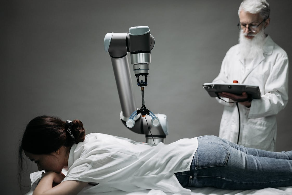 A woman lies face down on a table as a robotic arm hovers over her back. A man in a lab coat monitors a tablet nearby. Neutral setting.