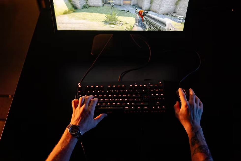 Hands on keyboard and mouse gaming in a dark room, with an FPS scene on the monitor and orange-lit keys