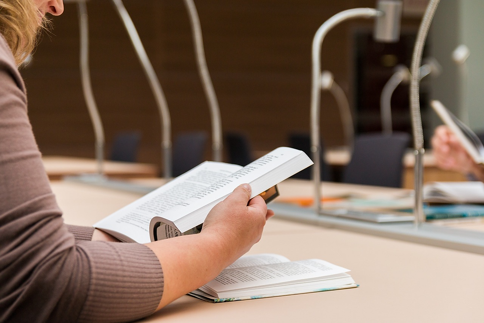 Person reading a book at a library table, surrounded by lamps. The setting is calm, with neutral tones and an academic atmosphere.