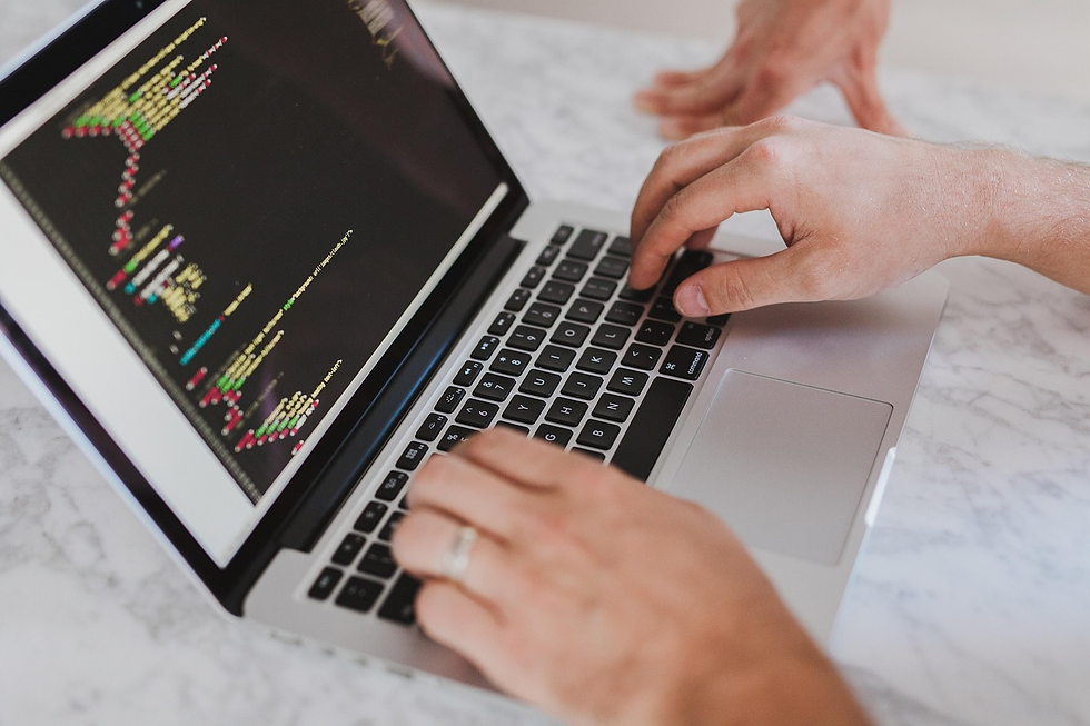 Hands typing code on a laptop with colorful text. Another hand suggests collaboration. Marble surface backdrop. Focused, tech-driven setting.