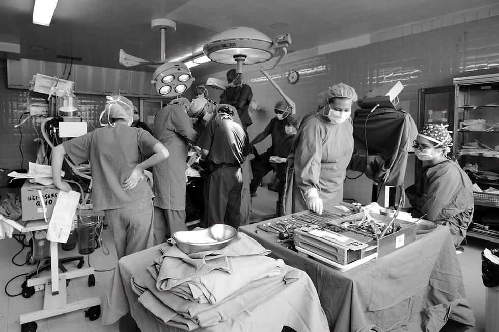 Medical team in scrubs performing surgery in an operating room. Surgical tools and equipment visible. Focused, intense atmosphere.