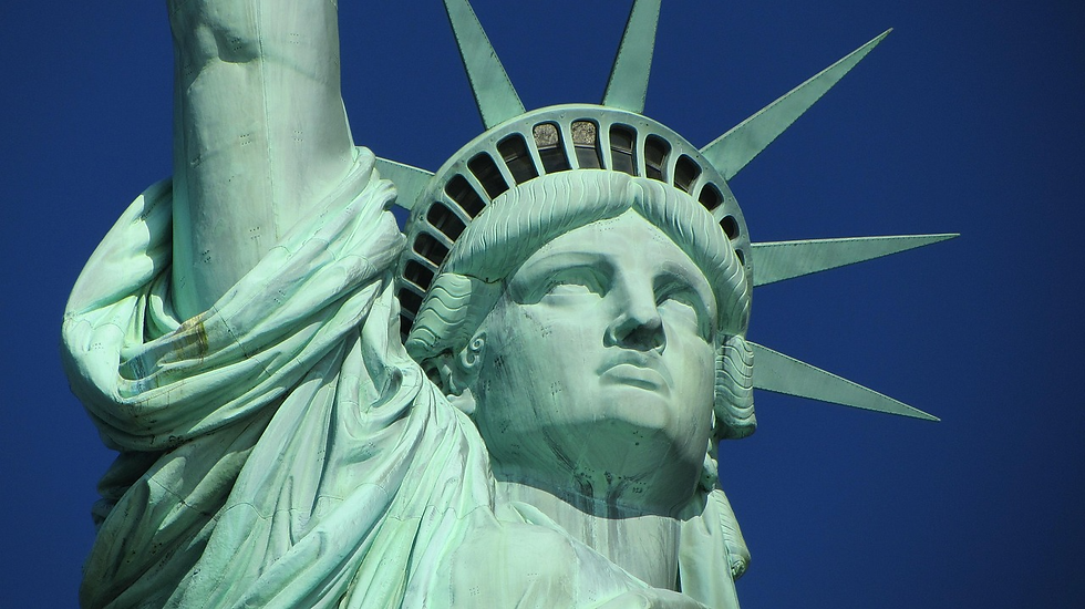 Close-up of the Statue of Liberty's face and crown against a clear blue sky. The iconic green patina is prominent, evoking a sense of freedom.