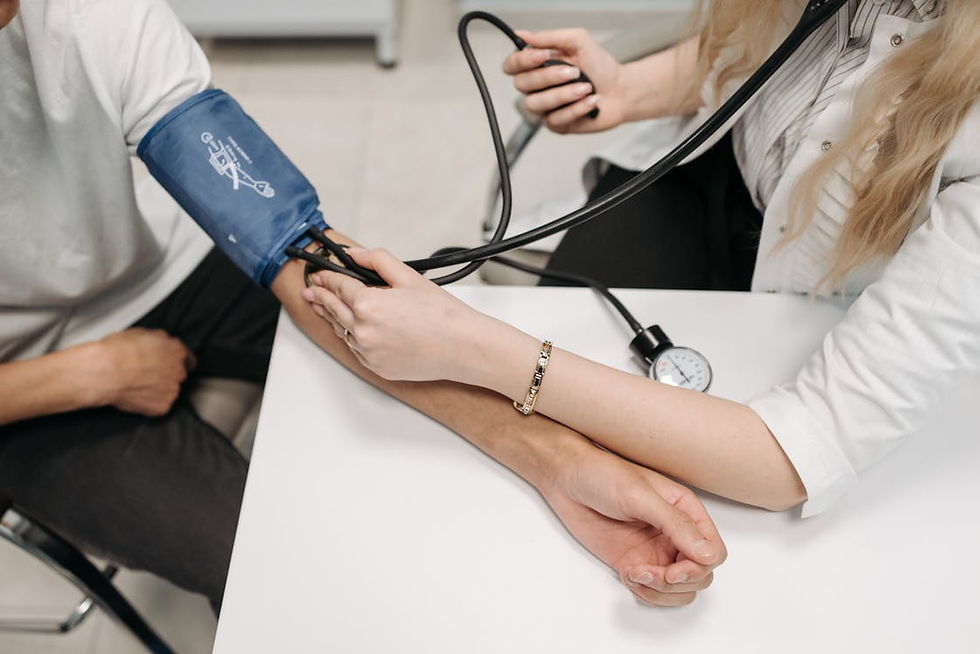 Healthcare worker measures a person's blood pressure with a blue cuff in a clinical setting. The gauge displays readings.